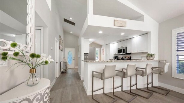 A modern kitchen with white cabinets, a central island with bar stools, and a decorative mirror. - CENTRALLY located house. (Naples)