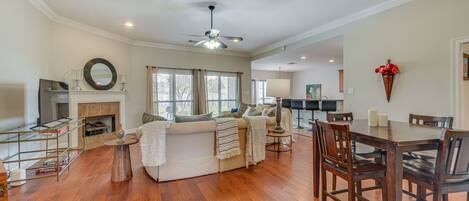 A spacious living room with a fireplace, a dining area with wooden chairs, and a ceiling fan.