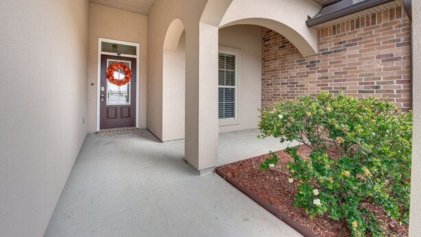 A covered walkway leading to a door with a wreath, a brick wall, and a small garden area. - Spacious Zachary Home: 12 Mi to Baton Rouge! (Zachary)