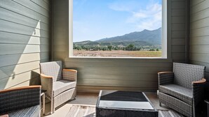 Ein Zimmer mit zwei Korbstühlen, einem kleinen Tisch und einem großen Fenster mit Blick auf die Berge.