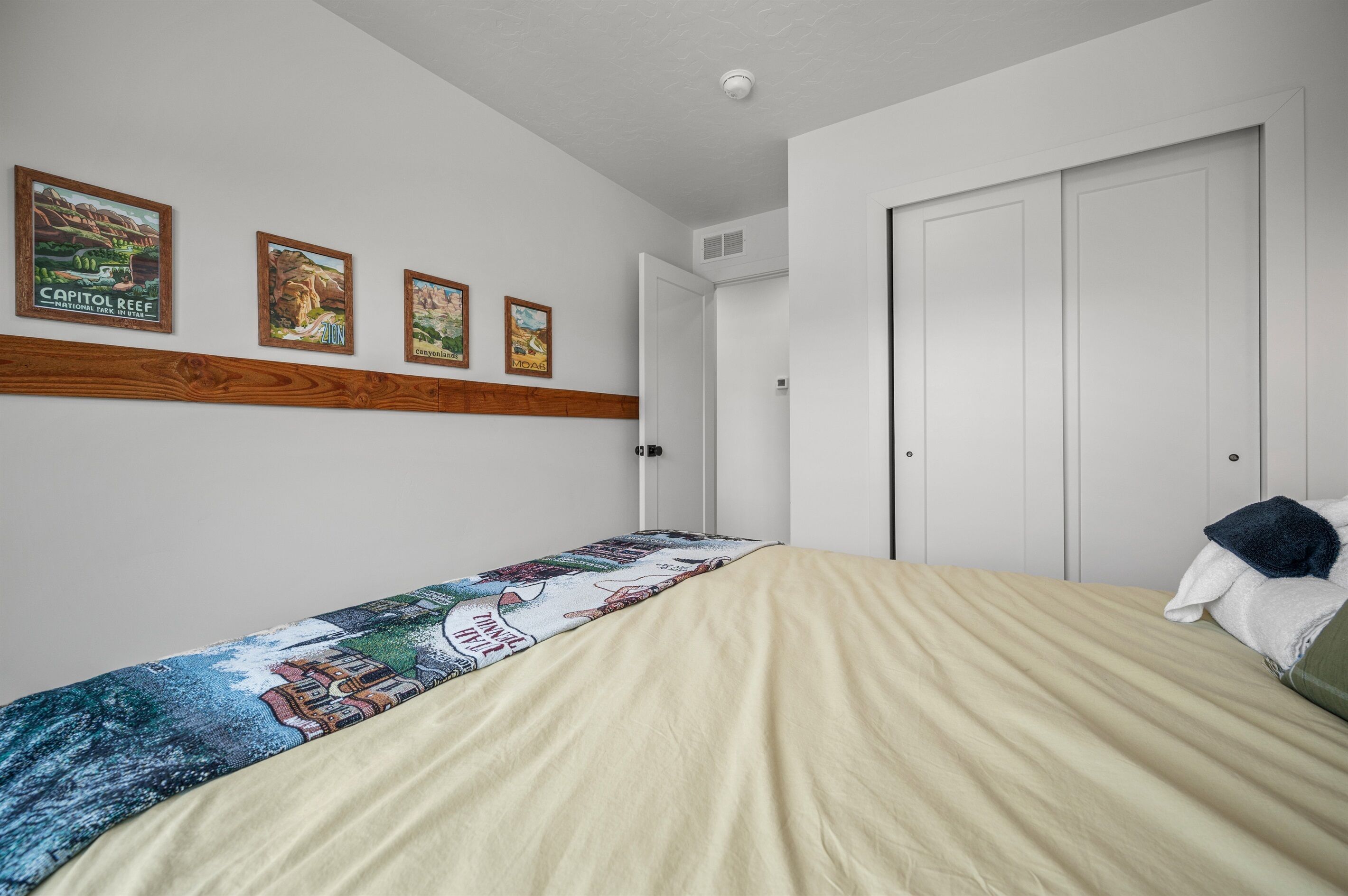 Une chambre à coucher avec un lit, une tête de lit en bois, un mur orné de posters encadrés et une porte blanche.