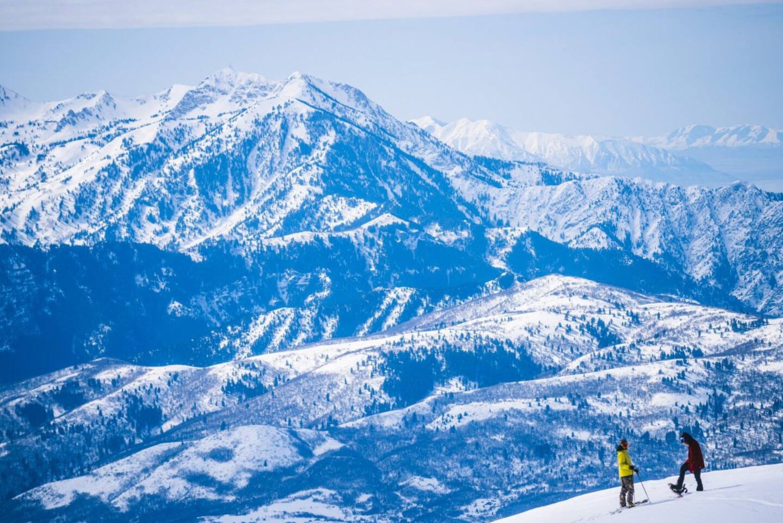 A snowy mountain landscape with two skiers in the foreground.