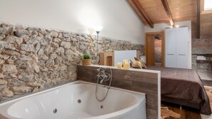 A bathroom with a stone wall, a bathtub, a wooden bench, and a bed with a brown bedspread. - Modernidad y Tradicion se Fusionan en Este Estudio en Santander (Santander)