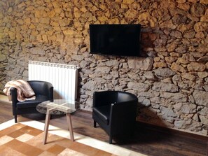 A room with a stone wall, a black chair, a glass table, and a black sofa. - Modernidad y Tradicion se Fusionan en Este Estudio en Santander (Santander)