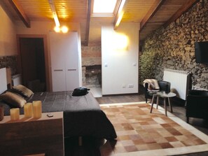 A cozy room with a bed, a small table, a chair, and a stone wall. - Modernidad y Tradicion se Fusionan en Este Estudio en Santander (Santander)