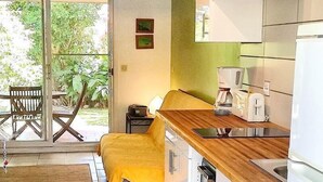 Une cuisine compacte dotée d’un plan de travail en bois, de meubles blancs et d’une porte-fenêtre coulissante donnant sur un espace extérieur avec une table et des chaises.