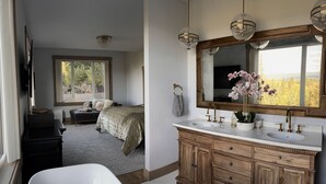 Une chambre avec une grande fenêtre, un lit, une coiffeuse avec un miroir et une baignoire.