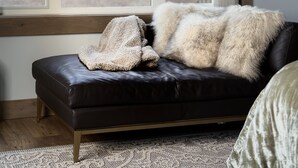 Une pièce dotée d’une grande fenêtre, d’un canapé en cuir noir et d’un plaid blanc et moelleux.