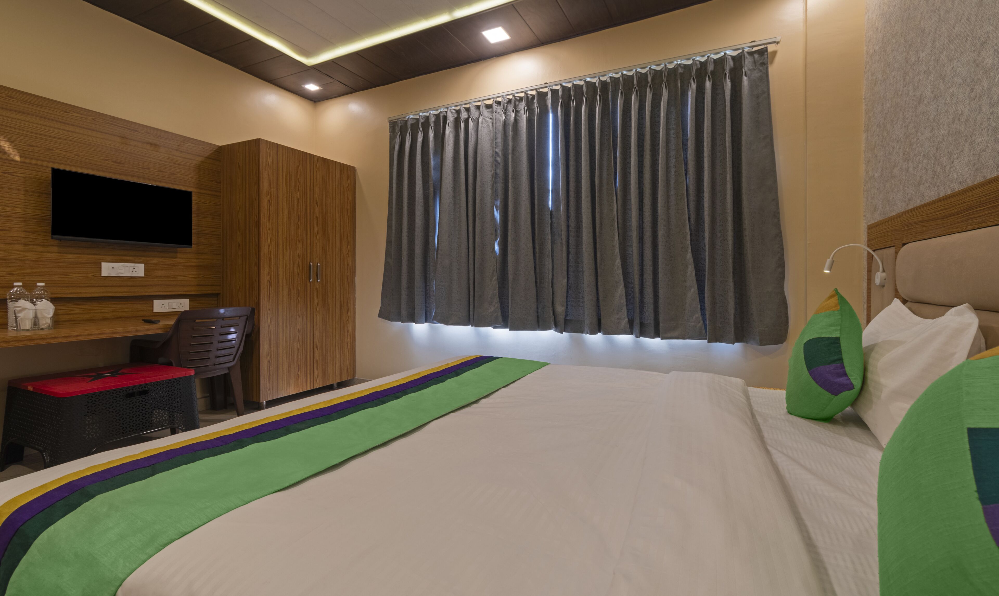 Habitación de hotel con cama, escritorio, silla, televisión y ventana con cortinas.