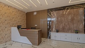Un espace d’accueil moderne avec un comptoir de réception en bois, une horloge et un mur en marbre.