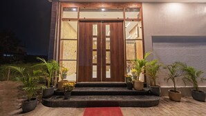 Une entrée moderne avec une porte double en bois, des plantes en pot et un tapis rouge menant aux marches.