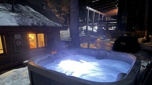 A hot tub surrounded by snow, with a wooden cabin in the background.