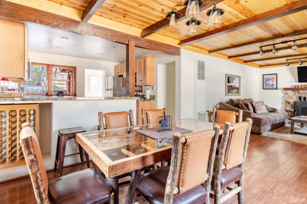 Una cocina amplia con vigas de madera, un comedor con mesa de vidrio y una sala de estar acogedora con chimenea.