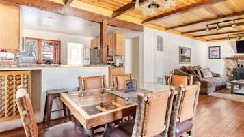 Una cocina amplia con vigas de madera, un comedor con mesa de vidrio y una sala de estar acogedora con chimenea.