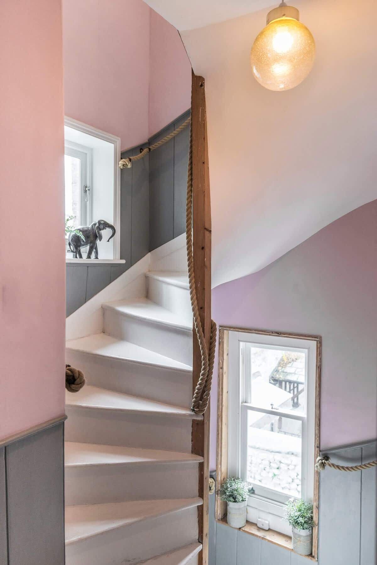 Un escalier avec une rampe en bois, un luminaire au-dessus et une petite fenêtre ornée d’une plante.