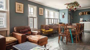 A spacious living room with a leather sofa, a yellow armchair, and a dining table with wooden chairs. - Old Post Office - Large house with games room +bar (Ramsgate)