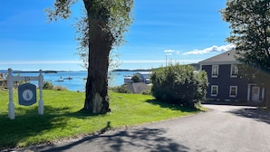 A coastal property with a paved driveway leading to a house, a sign indicating 'Seabreeze on the Harbor', and a view of the sea with boats.