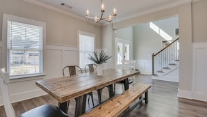 A dining area with a wooden table, benches, and chairs. There is a chandelier above the table. - Perfect Master's Rental (Grovetown)