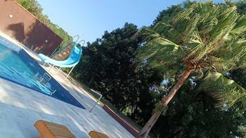 Una piscina con un tobogán azul, rodeada de palmeras y un cielo despejado.