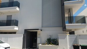 Un bâtiment moderne à la façade plate, doté de balcons avec des garde-corps en verre et d’une petite entrée avec une porte.