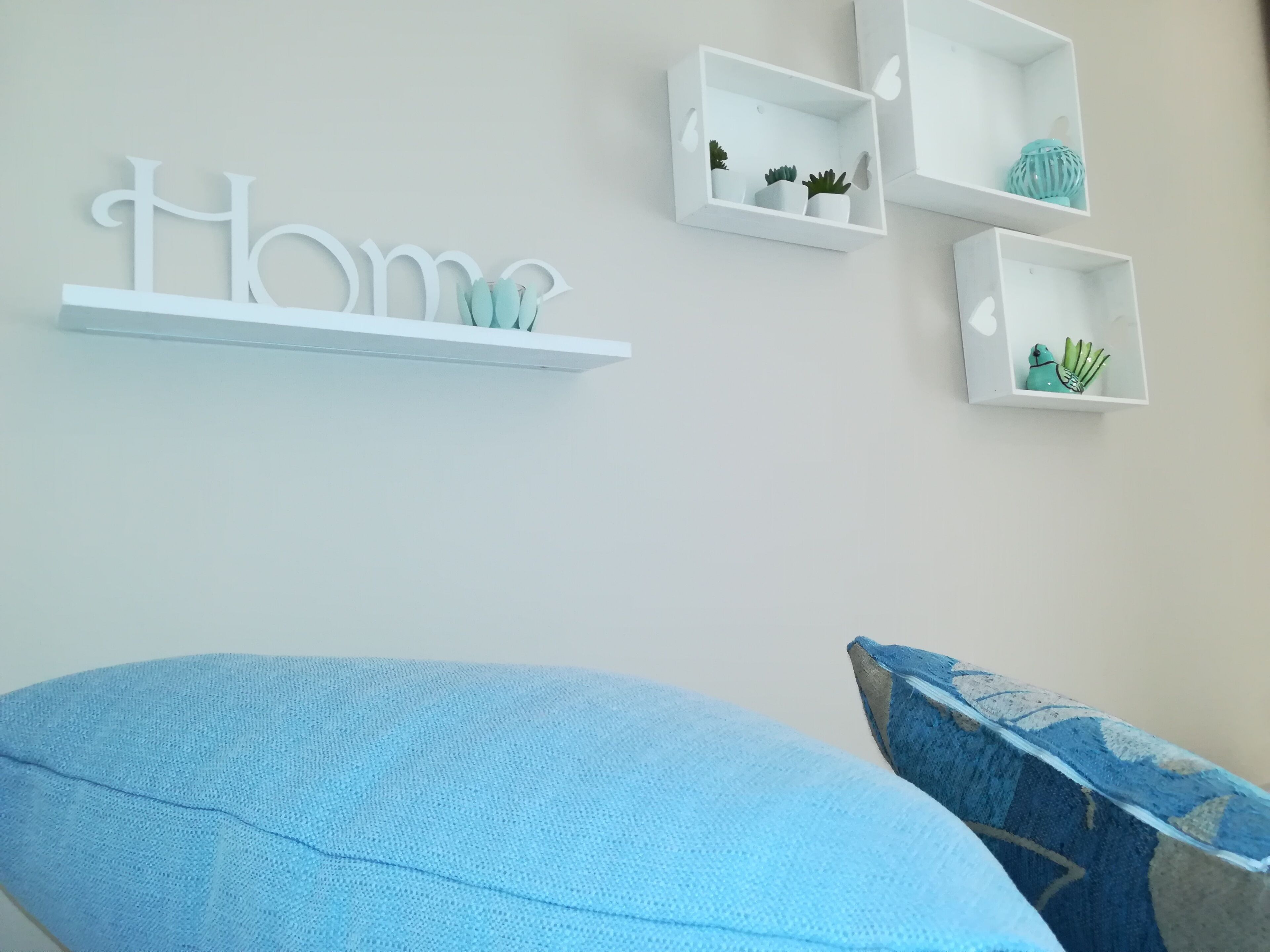 A bedroom with a bed, a wall-mounted shelf with decorative items, and a wall with a large word 'Home'.