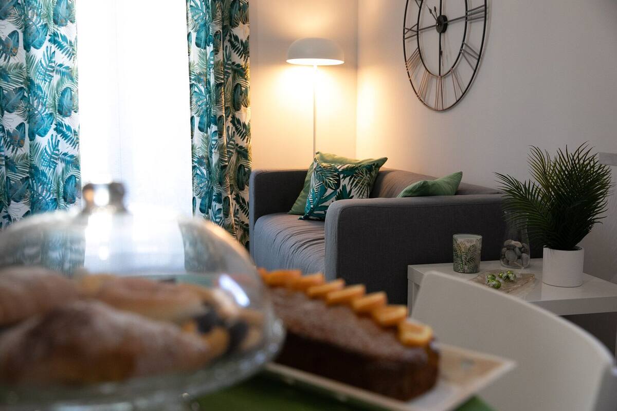Una sala de estar moderna con un sofá, una lámpara, un reloj y una mesa con un pastel y objetos decorativos.