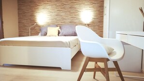 Une chambre à coucher moderne avec une tête de lit en bois, un lit blanc et un bureau blanc avec une chaise.