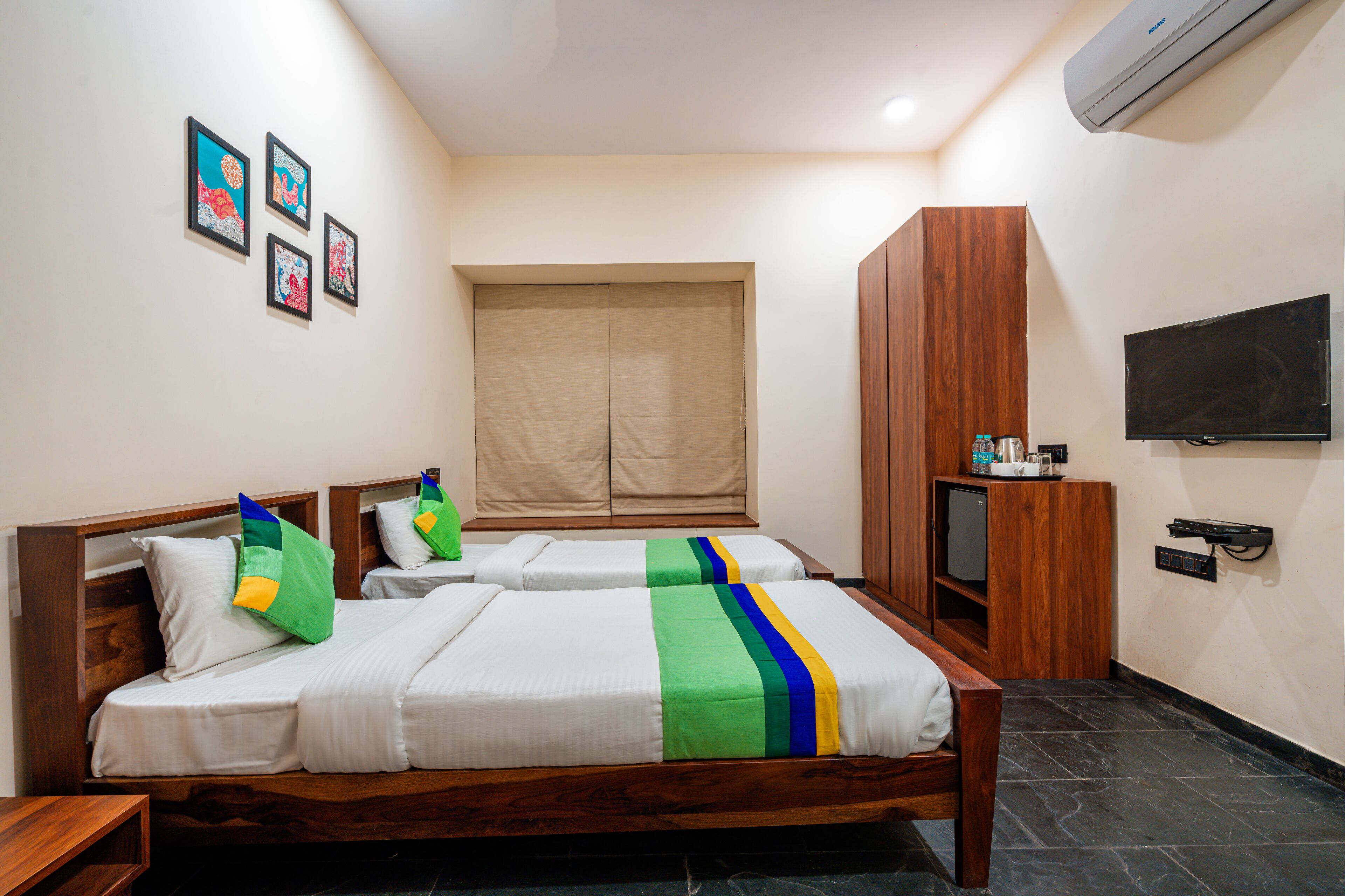 A hotel room with two beds, a wardrobe, a television, and artwork on the wall.
