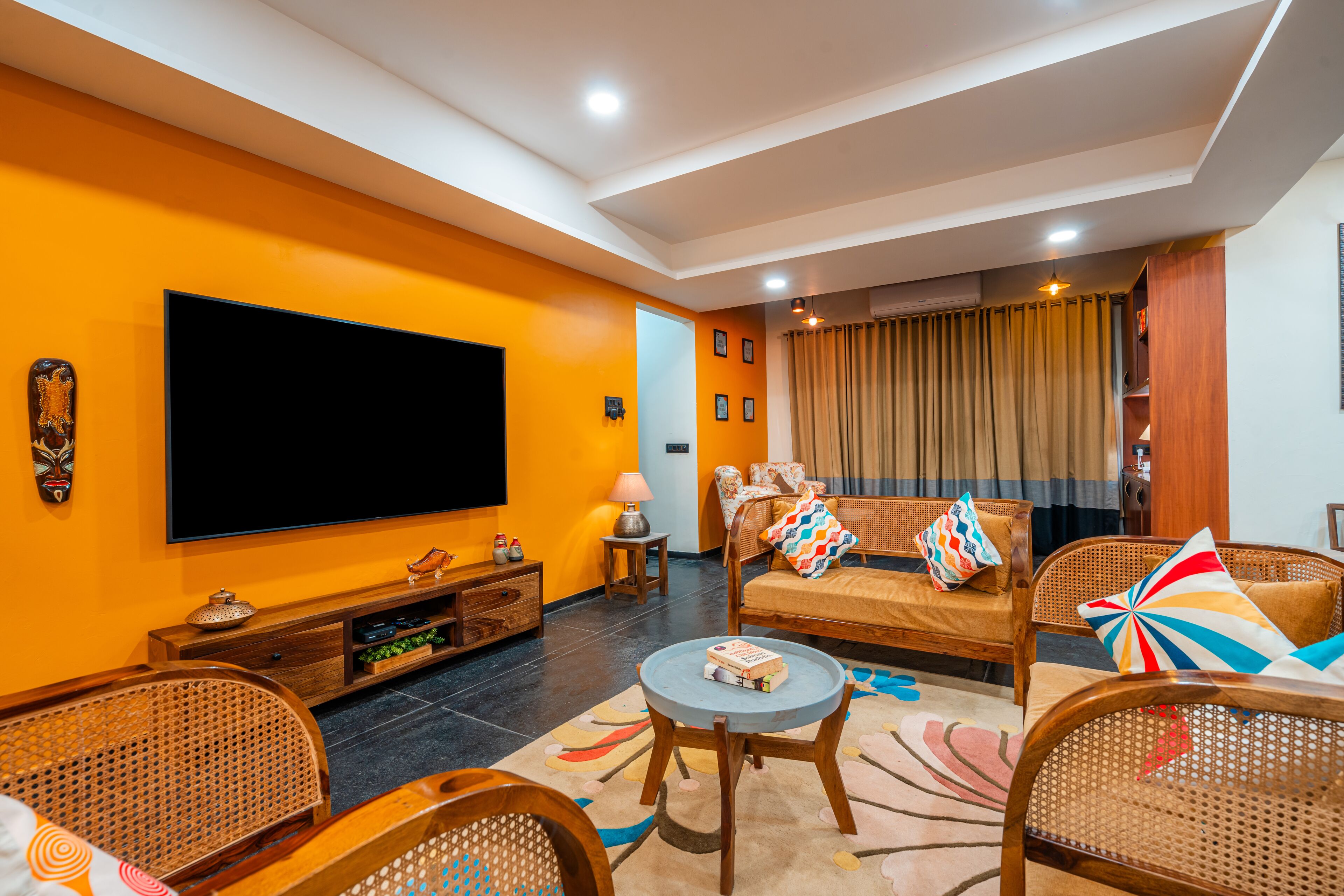 A living room with a large flat-screen TV, wooden furniture, and a colorful rug.