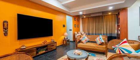 A living room with a large flat-screen TV, wooden furniture, and a colorful rug.