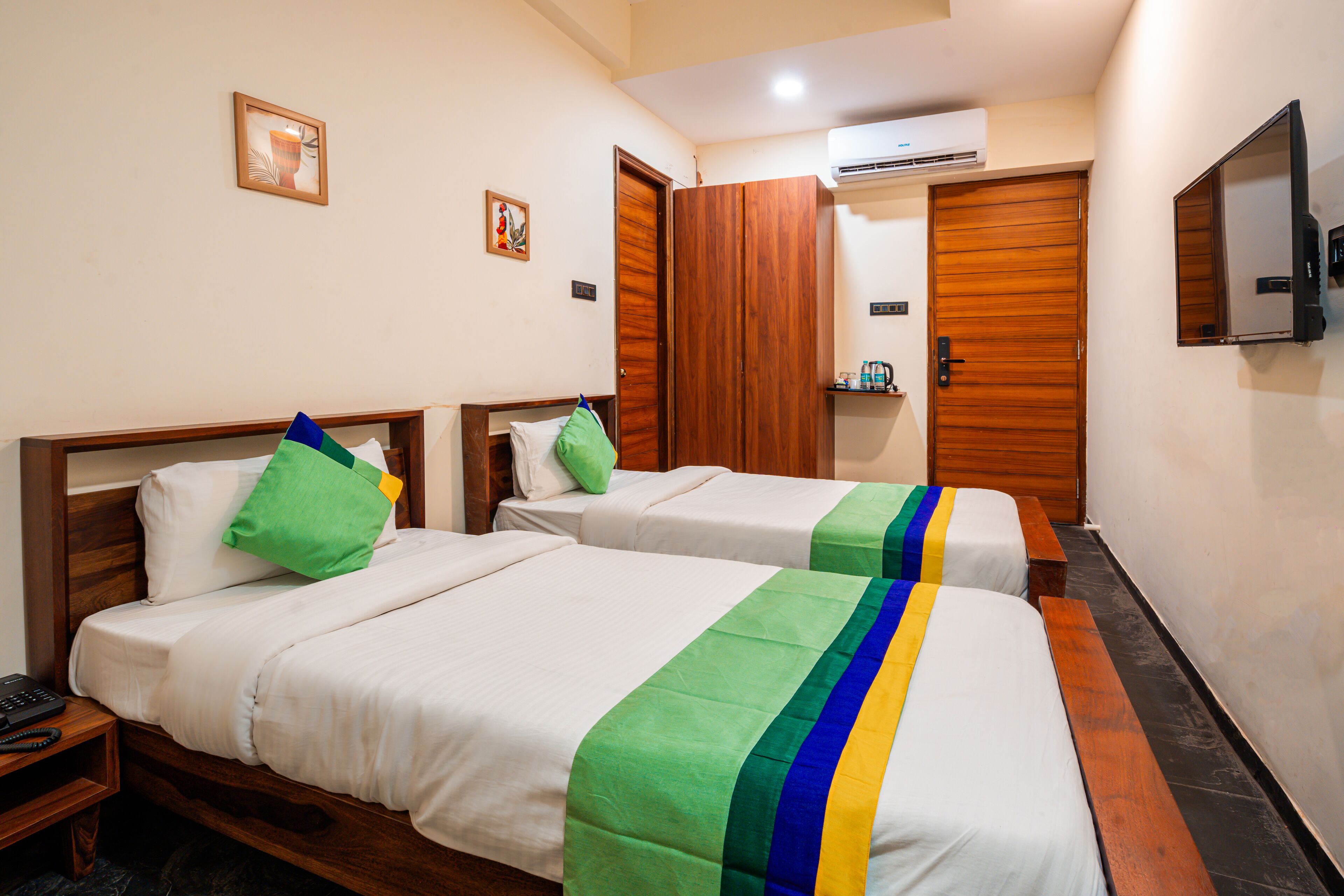 A hotel room with two single beds, a wooden wardrobe, a small table with a phone, and a mounted TV.