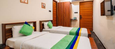 A hotel room with two single beds, a wooden wardrobe, a small table with a phone, and a mounted TV.