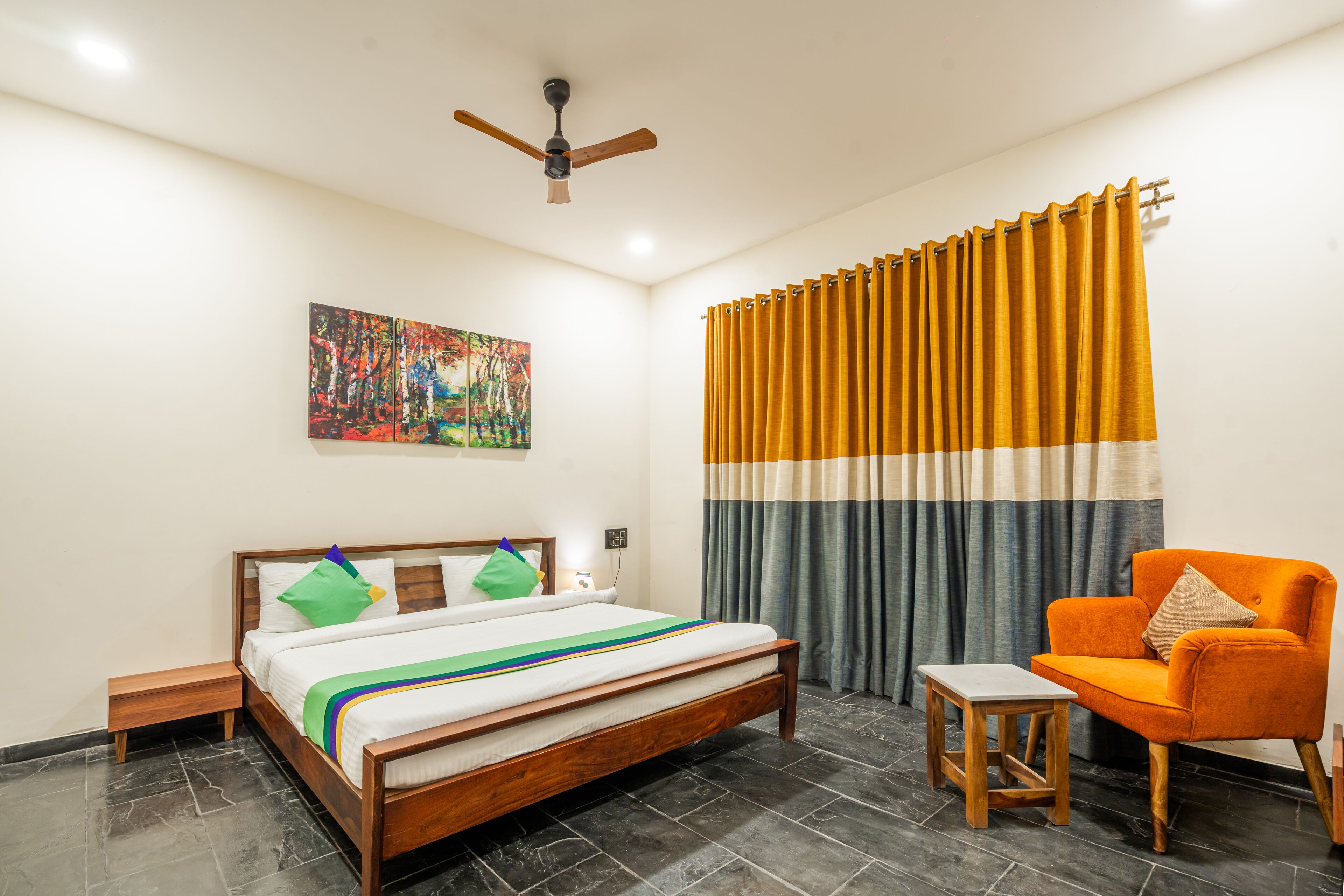 Quarto com cama, cadeira, mesa de cabeceira, ventilador de teto e um quadro na parede.