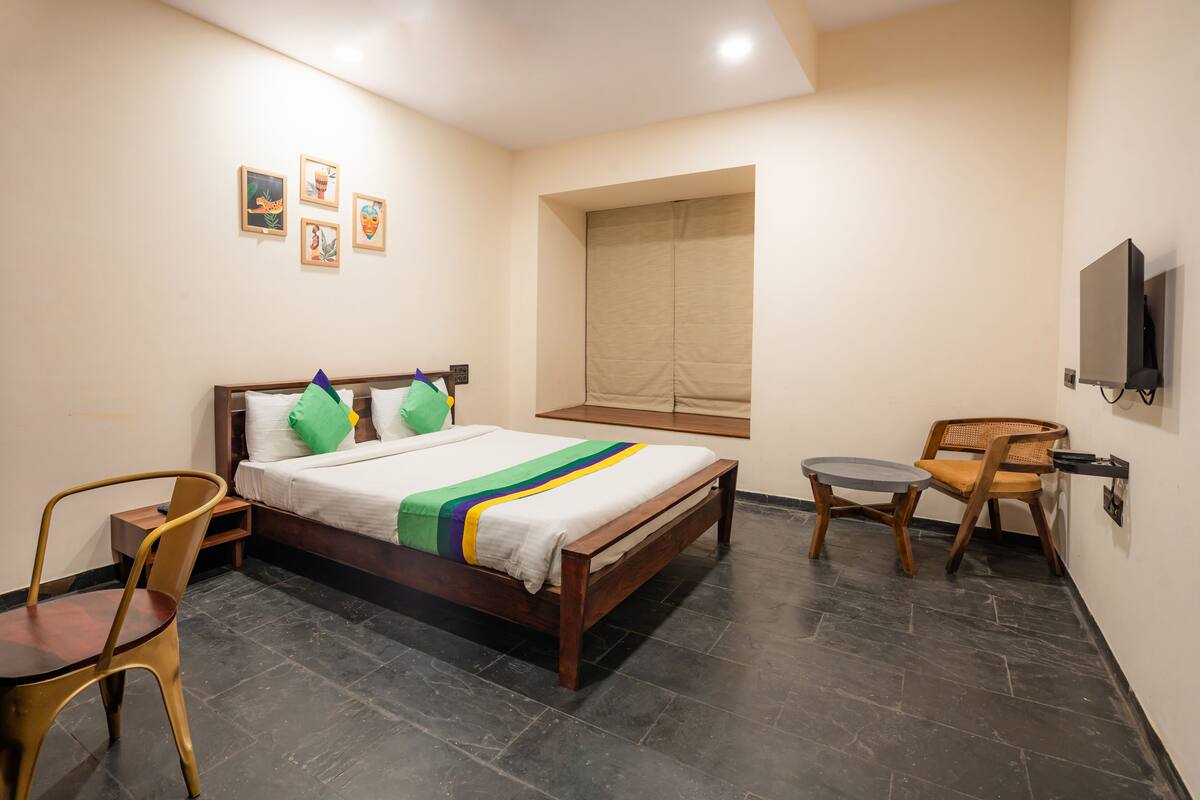 A hotel room with a bed, a desk, a chair, a TV, and artwork on the wall.
