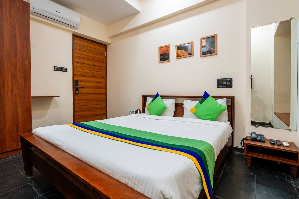 A neatly made bed with a white and green striped bedspread, a wooden headboard, and a bedside table with a phone and a lamp.