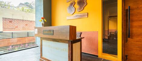 A reception desk with a wooden finish, a vase with flowers, and a yellow wall with wooden art pieces.