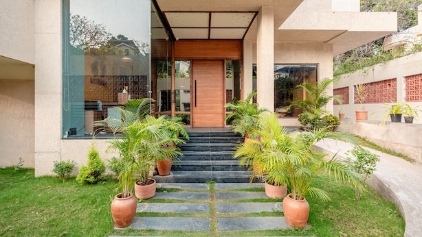 A modern building entrance with a wooden door, potted plants, and a stone pathway leading to the entrance. - Treebo Premium The Memoir, Ramdaspeth (Nagpur)