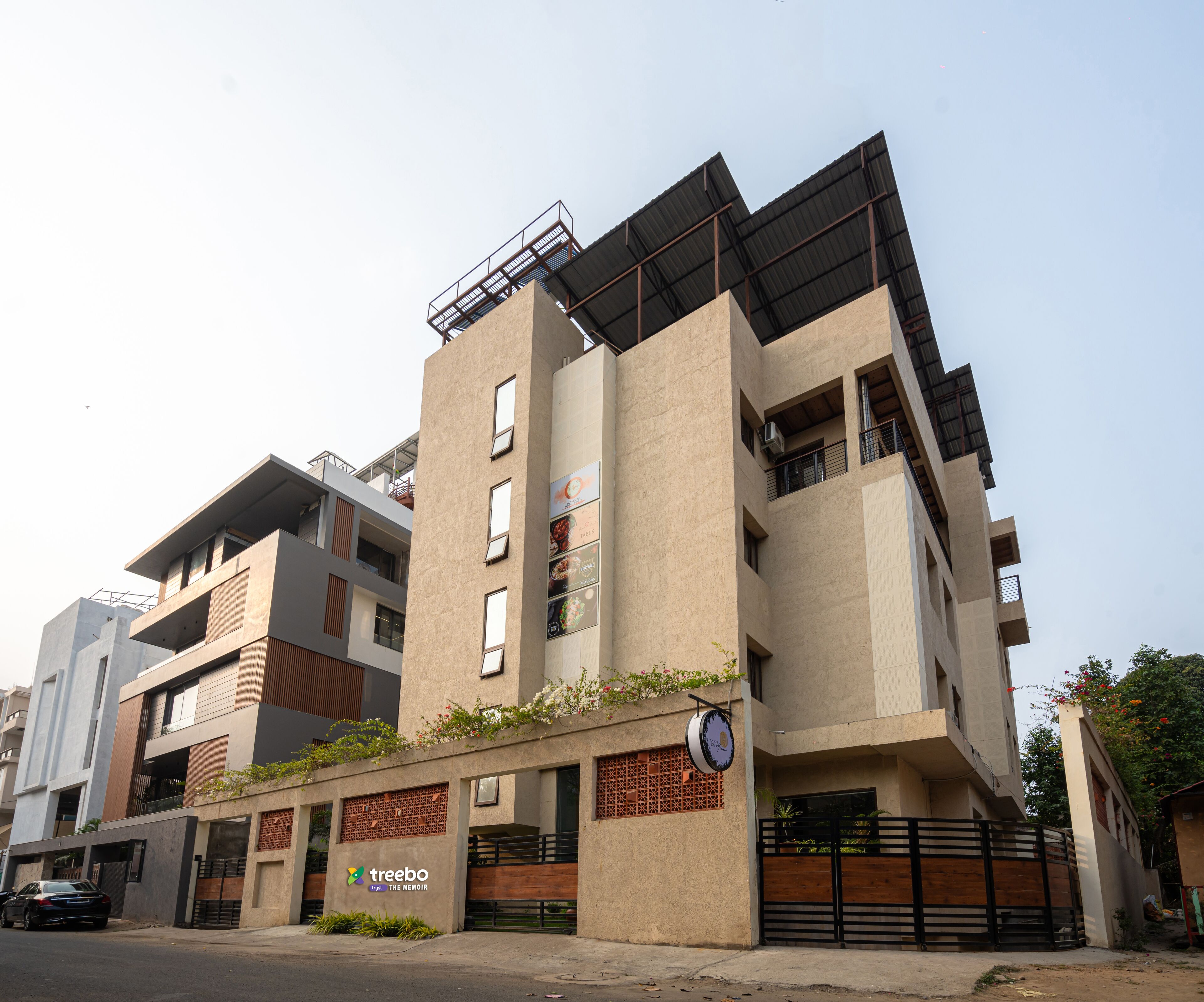 A multi-story building with a flat roof, large windows, and a sign for 'Treebo The Memoir'.