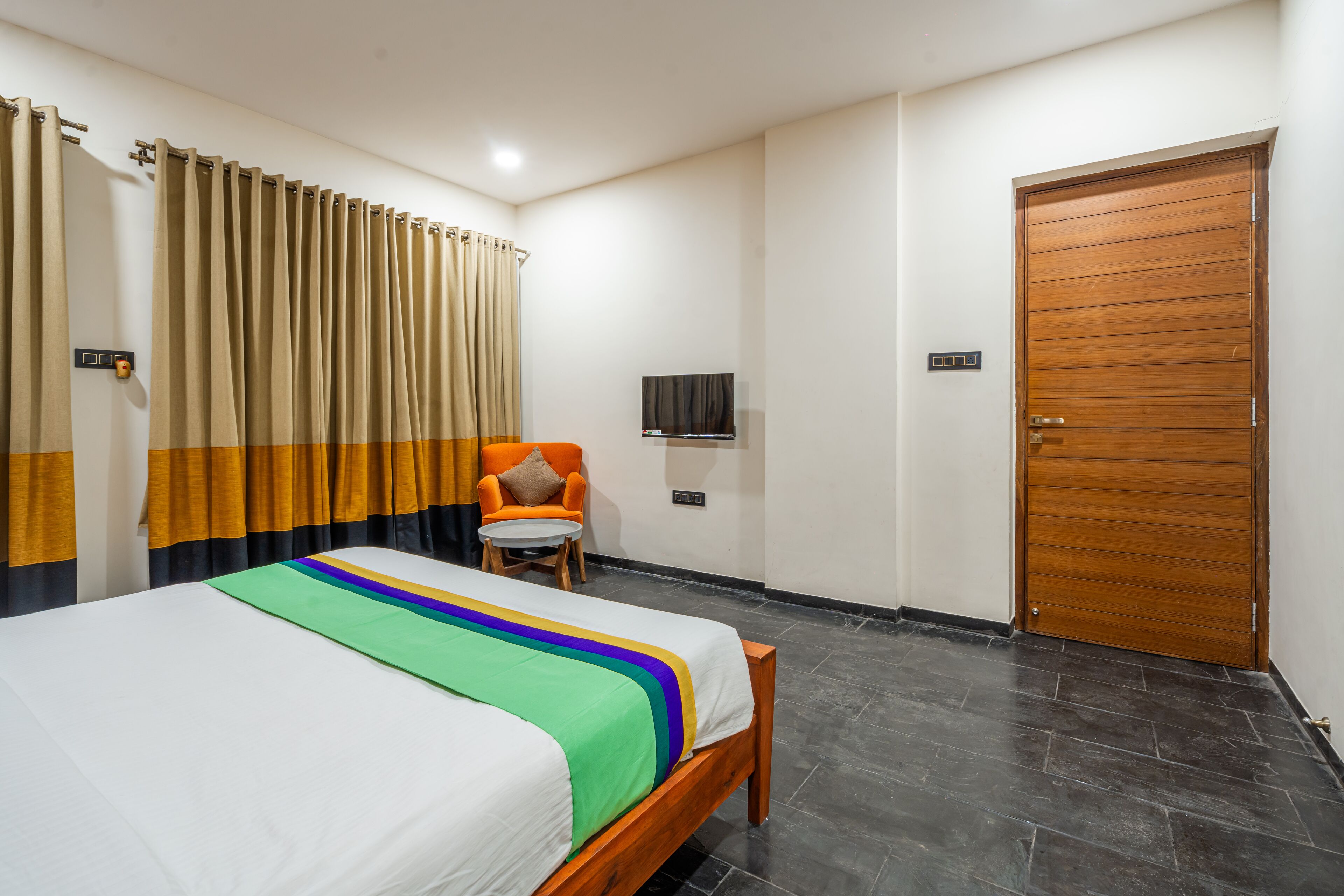 A hotel room with a bed, a chair, a television, and a wooden door.