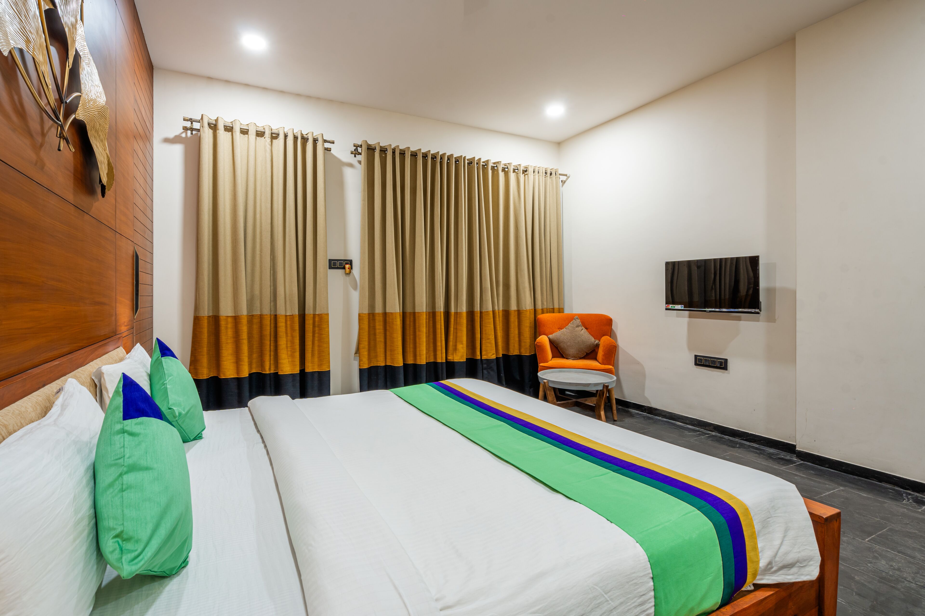 Ein Hotelzimmer mit einem großen Bett, einem Sessel, einem Fernseher und Vorhängen.