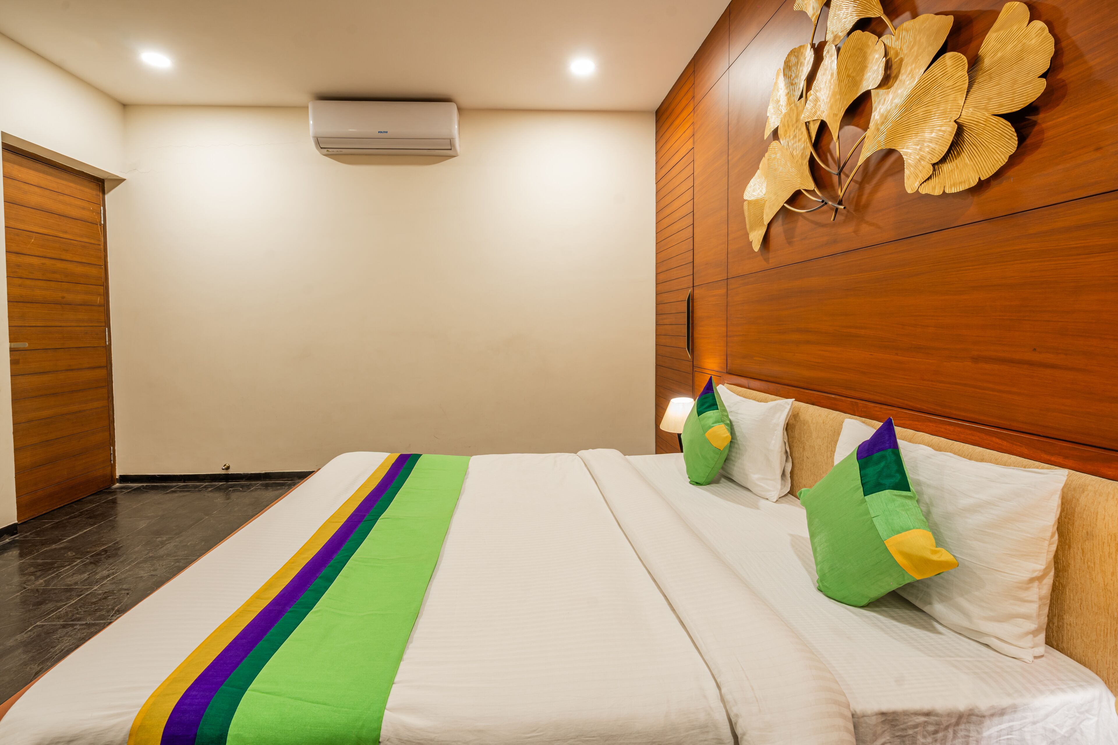 A hotel room with a bed, wooden headboard, and a wall-mounted air conditioner.