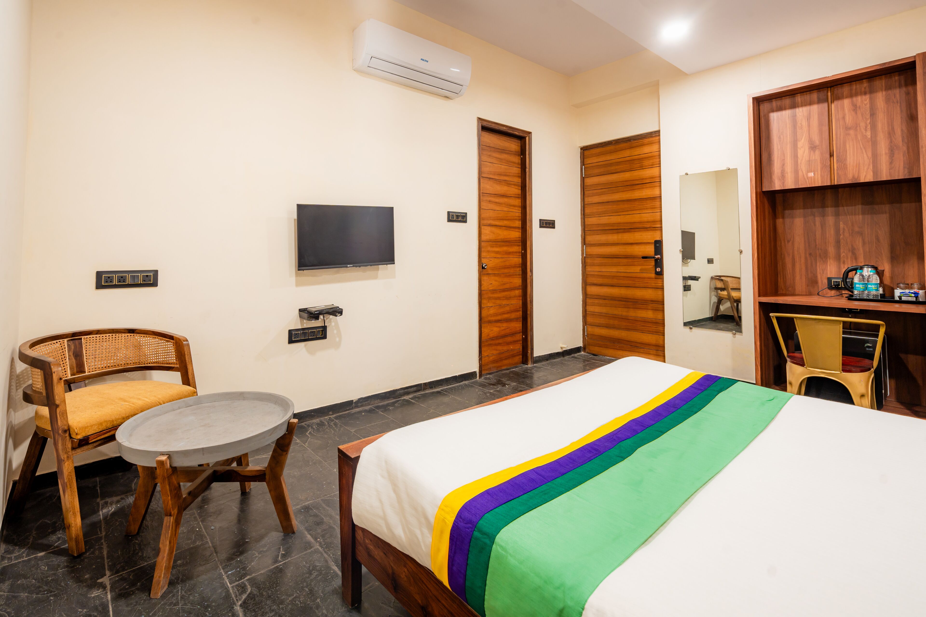 A hotel room with a bed, a television, a wooden wardrobe, a small round table, and a chair.
