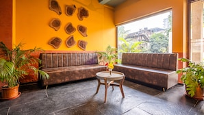 A room with a brown leather sofa, a round wooden table, and a large window with a view of buildings and greenery. - Treebo Premium The Memoir, Ramdaspeth (Nagpur)