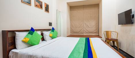 Une chambre d’hôtel avec un grand lit, une tête de lit en bois, une chaise, un téléviseur et trois tableaux encadrés accrochés au mur.