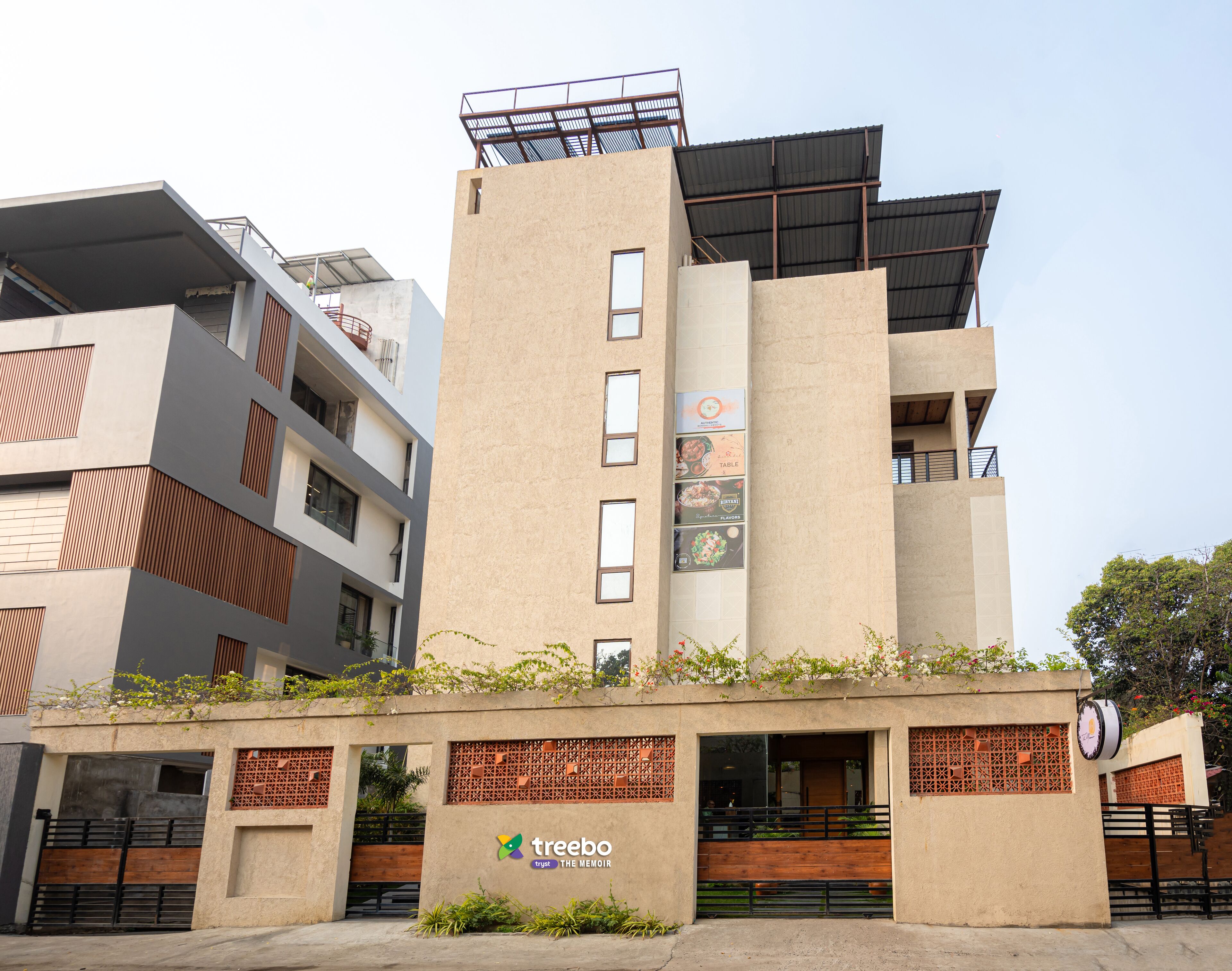Un edificio moderno con tetto piatto e numerose finestre, con un'insegna che riporta 'Treebo Trust The Memoir'.