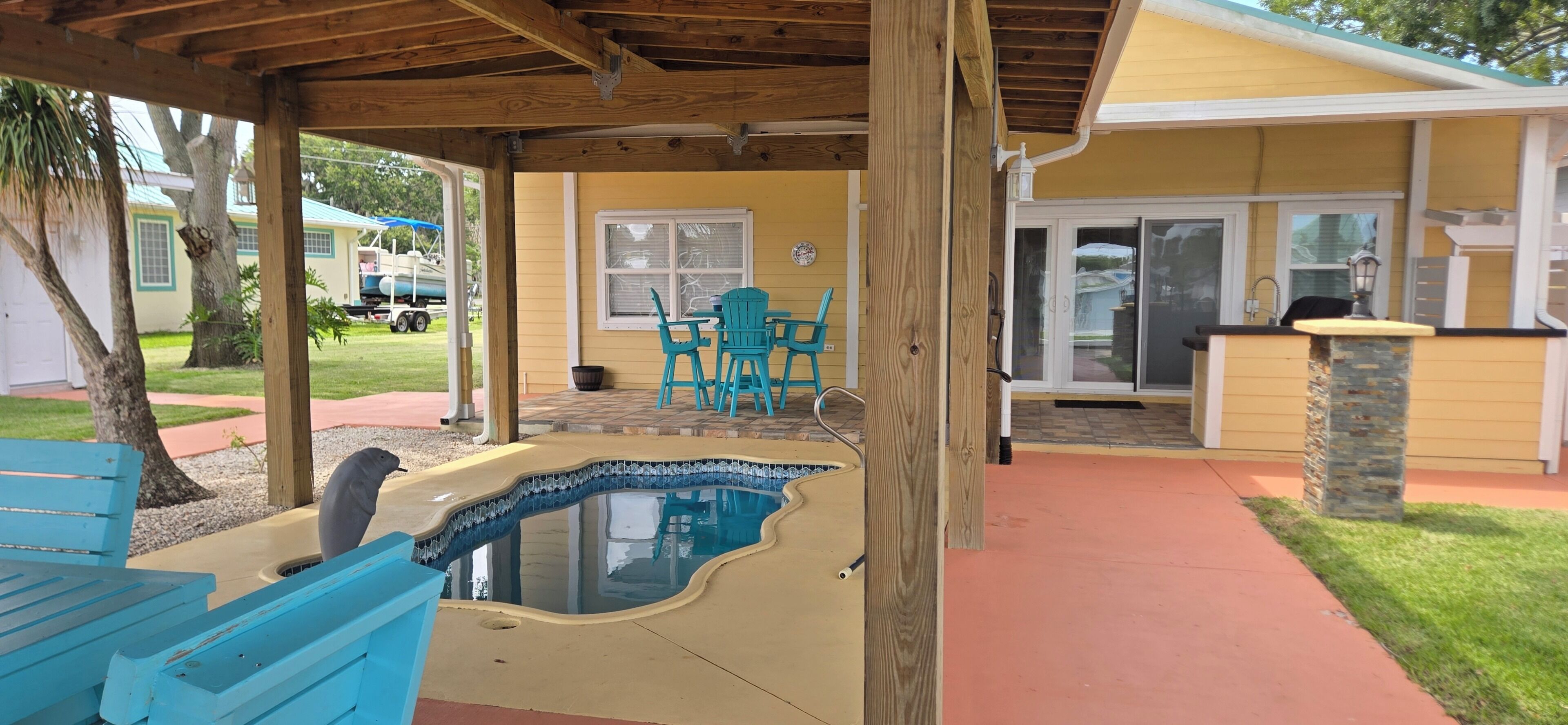 A covered patio area with a small pool, outdoor seating, and a house in the background.
