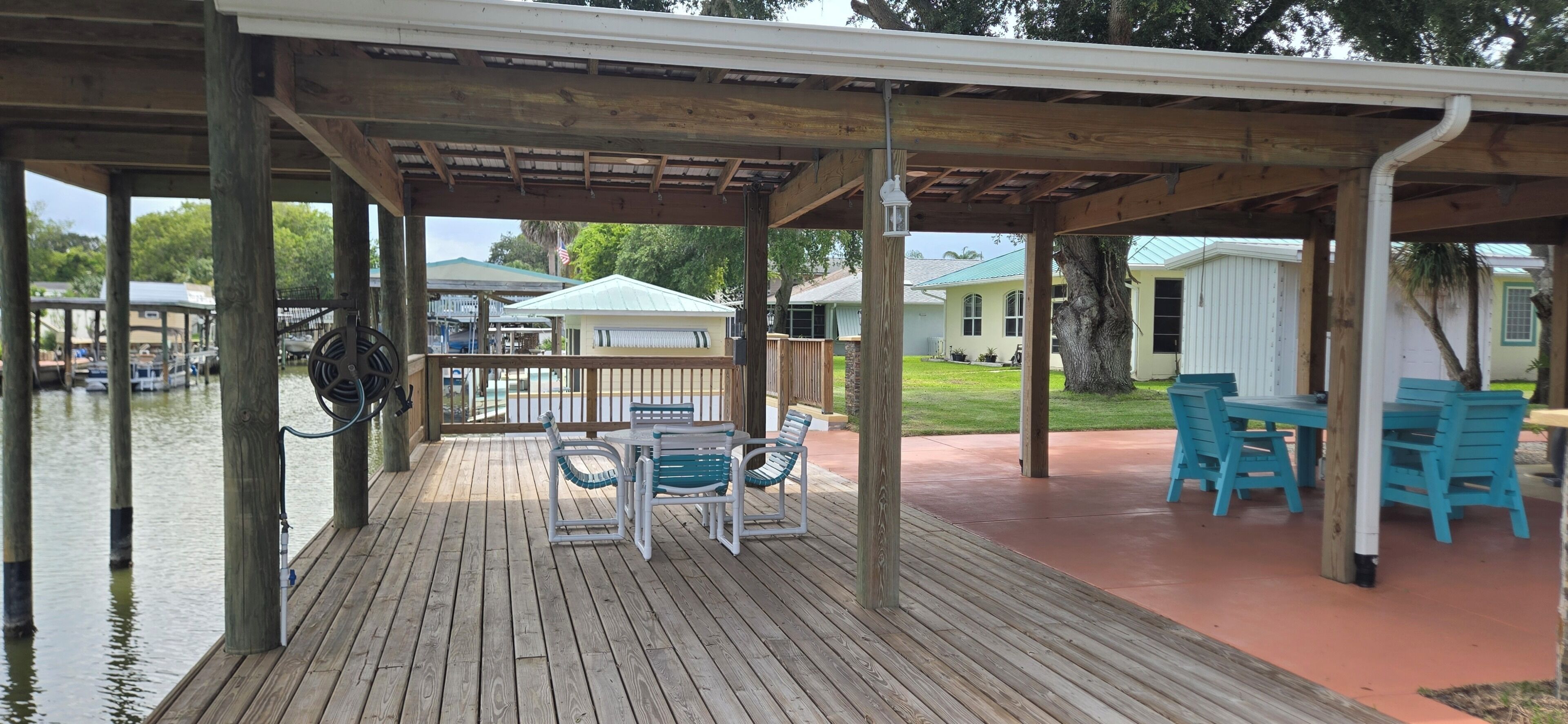 A covered outdoor deck with a table and chairs, a wooden railing, and a view of a house and water.