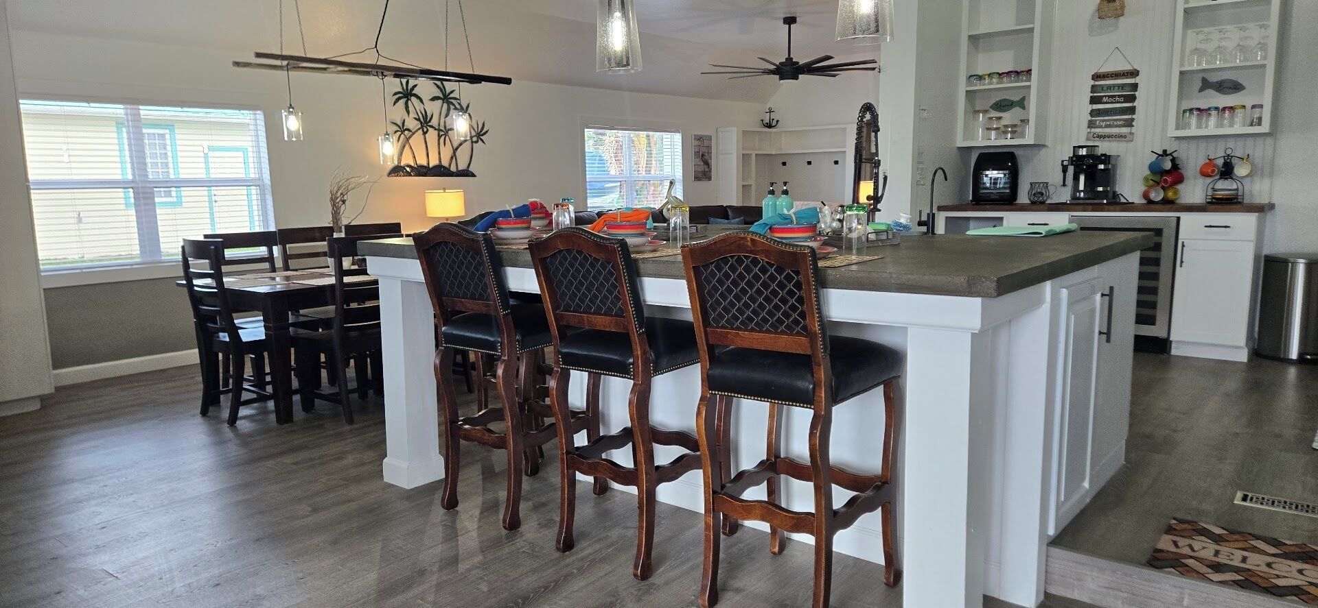 A modern kitchen with white cabinets, a central island with bar stools, and a dining area with wooden chairs.