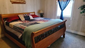 Una cama de madera con un colcha colorida, una mesita de noche pequeña y una ventana con cortinas.