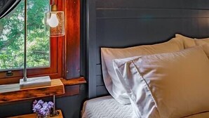 Une chambre à coucher avec un lit, une table de chevet, une lampe et une fenêtre avec des rideaux.